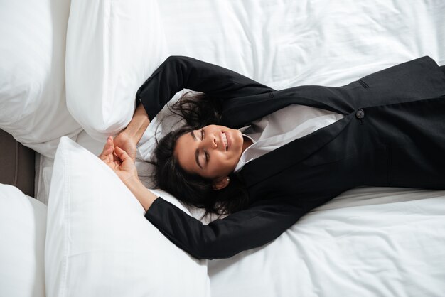 Happy exhausted businesswoman lying in bed in room