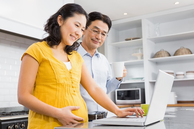 Happy expectant couple using laptop in the kitchen