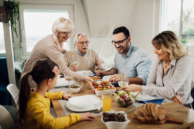 Happy extended family having lunch together in dining room Senior woman is serving food at the table