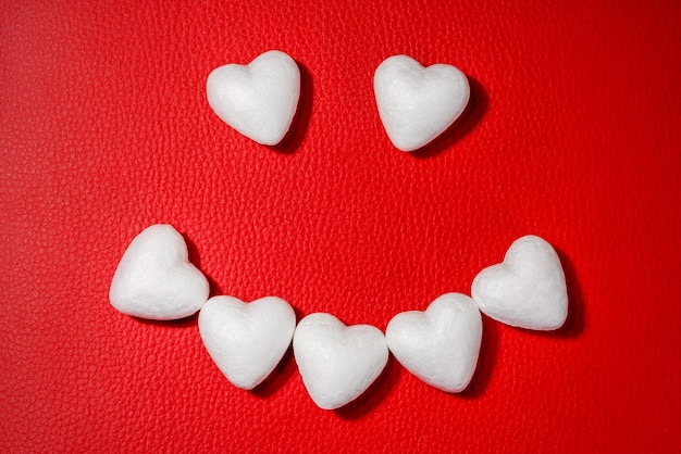 Счастливое лицо, сделанное из белых сердец на красном кожаным фоне.