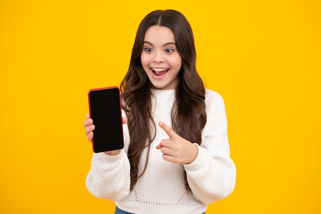 Happy face positive and smiling child girl 12 13 14 years old with smart phone hipster teen girl types text message on cellphone mobile app kid showing blank screen mobile phone copyspace
