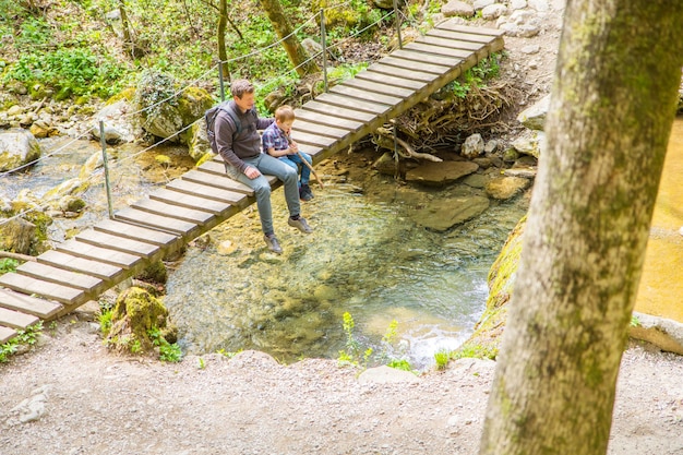 Happy family are sitting on a wooden bridge in the middle of forest