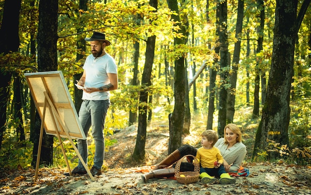 Happy family. Artist father Drawing own Family from nature. with a beard in a hat, creating a canvas. Artist services. Canvas instead of photos.