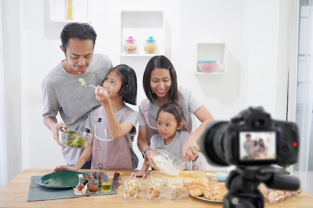 Asiatico felice della famiglia che fa una macchina fotografica digitale di video blogger di vlog con la cottura nella stanza della cucina