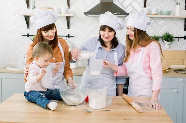 Happy family baking in the kitchen. Grandmother with her daughters and granddaughter preparing the dough, Granny pours milk from a bottle into a measuring glass