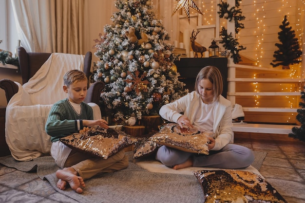 Felice ragazzo e ragazza di famiglia che decorano un albero di natale con palline e regali in soggiorno, buon natale e vacanze di capodanno. famiglia, vacanze invernali e concetto di persone