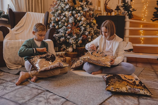 Felice ragazzo e ragazza di famiglia che decorano un albero di natale con palline e regali in soggiorno, buon natale e vacanze di capodanno. famiglia, vacanze invernali e concetto di persone