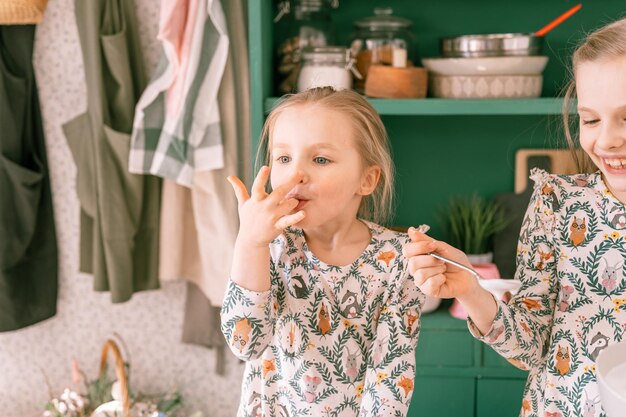 幸せな家族の率直な小さな子供姉妹の女の子は一緒にキッチンの装飾テーブルとイースターケーキベーカリー甘いアイシングとランチまたはディナーのためのキャンディーで自宅で楽しい春のイースター休暇を楽しんでいます