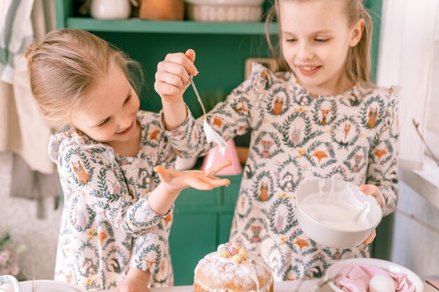 幸せな家族の率直な小さな子供姉妹の女の子は一緒にキッチンの装飾テーブルとイースターケーキベーカリー甘いアイシングとランチまたはディナーのためのキャンディーで自宅で楽しい春のイースター休暇を楽しんでいます