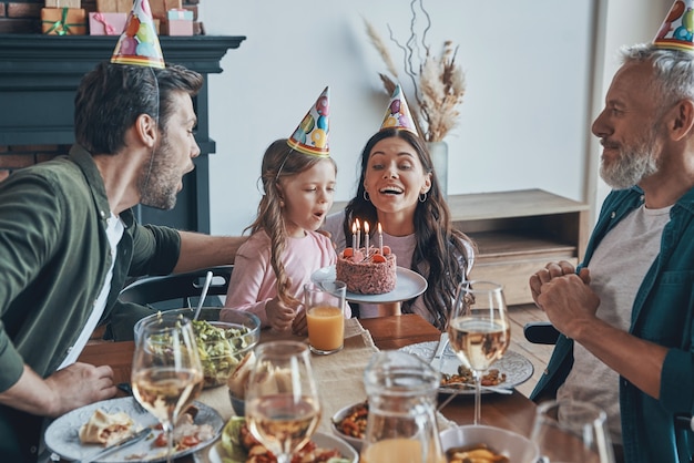 自宅の食卓に座って小さな女の子の誕生日を祝う幸せな家族