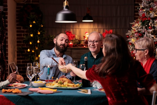 クリスマスを祝う幸せな家族、おしゃべり、ホームパーティーのお祝いのディナーテーブルで料理を食べる。美しい豪華な装飾が施された場所での両親とのクリスマス冬の休日のお祝い