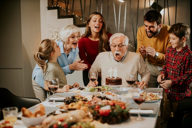 Happy family celebrating grandfather birthday with cake and candles at home