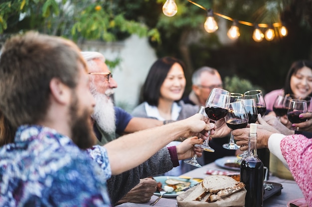 Happy family cheering with red wine at barbecue dinner outdoor - Different age of people having fun at weekend meal - Food and summer concept - Focus on close-up glass