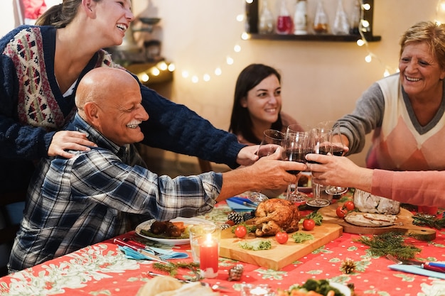 Счастливая семья аплодирует вином во время рождественского праздничного ужина вместе - сосредоточьтесь на руках, держащих очки