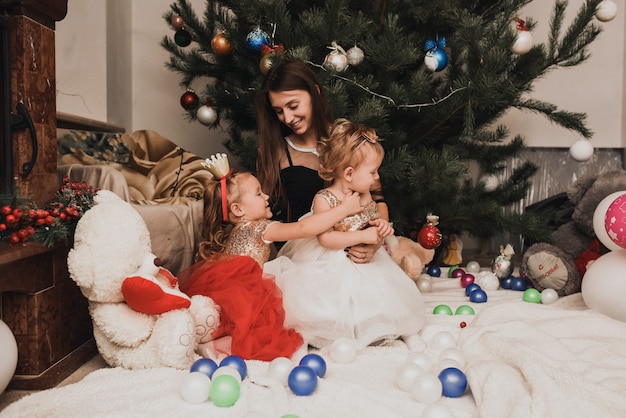 Счастливые семейные дети празднуют Новый год и Рождество на украшенной елке и гирляндах