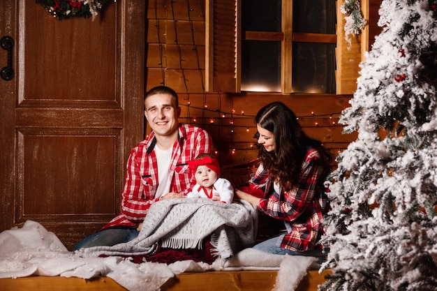 Happy family at Christmas eve sitting together near decorated tree at living room, home. Father, mother and baby girl.