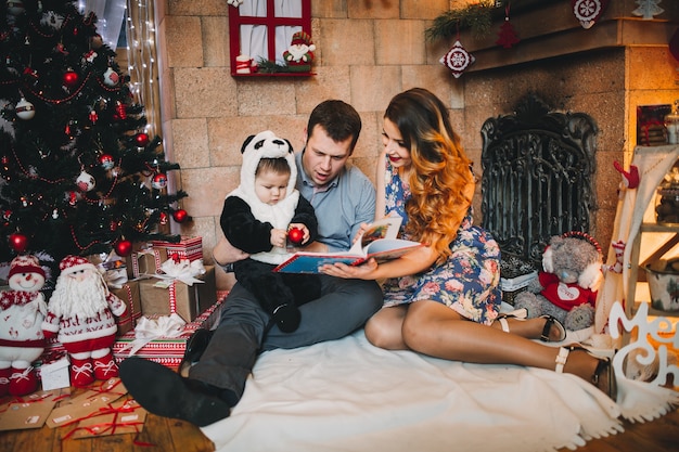 Happy family at Christmas and with gifts around the Christmas tree read book.