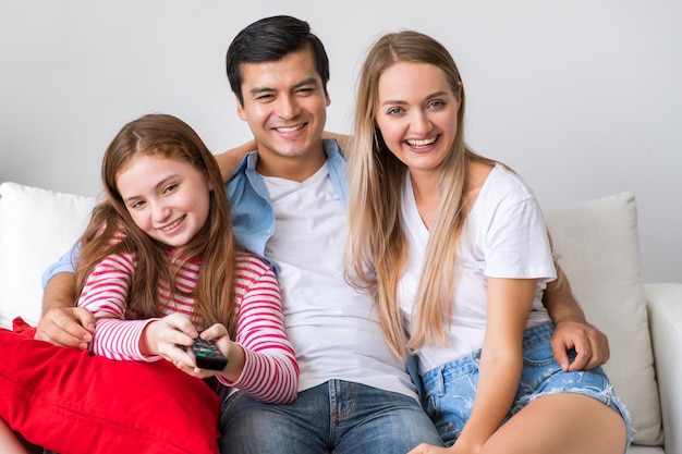 Happy family on couch in living room including father and
mother and daughter enjoy watching television together with remote
control