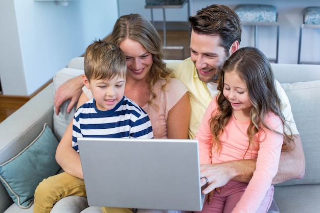 Famiglia felice sul divano insieme usando il portatile