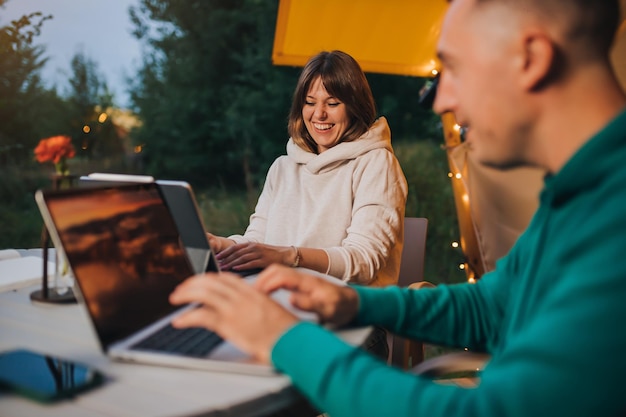 Happy family couple freelancers working laptop on a cozy\
glamping tent in summer evening luxury camping tent for outdoor\
holiday and vacation lifestyle concept