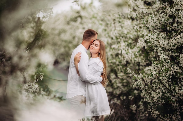 Счастливая влюбленная семейная пара в весеннем цветущем яблоневом саду Счастливая семья наслаждается друг другом во время прогулки в саду Мужчина держит женщину за руку Семейные отношения