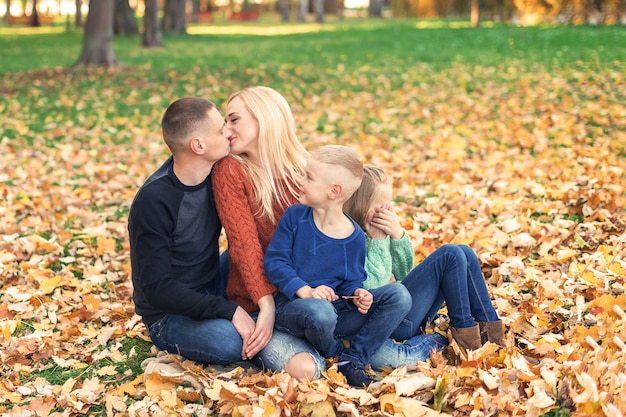 Happy family couple with children kissing in autumn park.