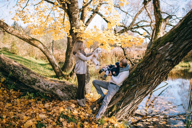 Happy family couple with their little child and puppy in autumn park in sunny day.