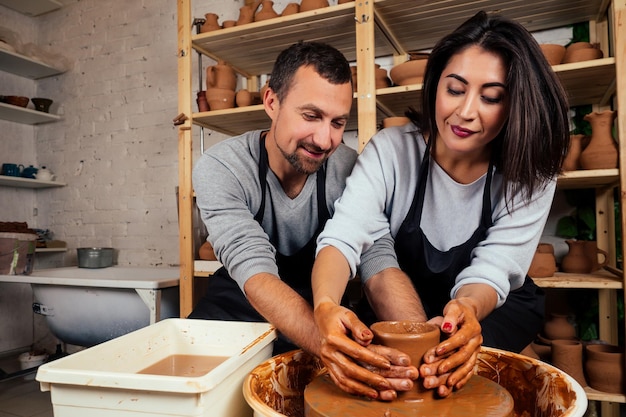 Happy family on a creative joint vacation. romantic couple in love working together on potter wheel and sculpting clay pot,a bearded man and a young woman mold a vase in craft studio workshop.