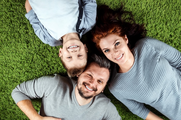 happy family, dad mom and son are smiling lying on a green carpet