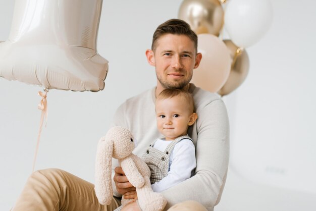 Happy family dad and one year old son sitting in the background of birthday balloons