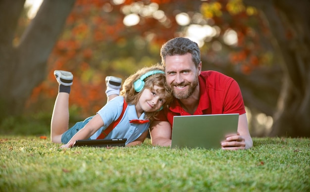 Счастливая семья папы и сына использует ноутбук для видеозвонка или урока, слушает музыку в наушниках в парке счастья