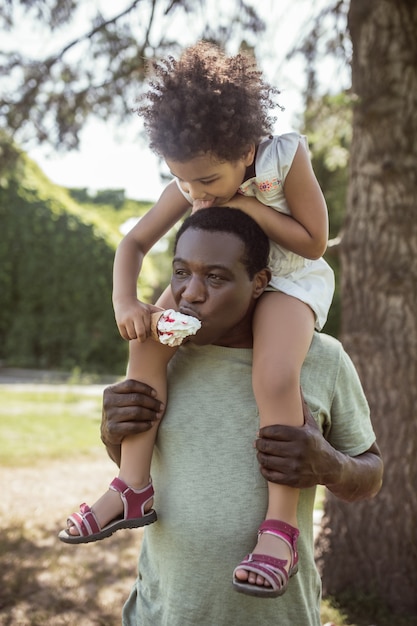 Happy family. Dark-skinned cute kid sitting on her dads shoulders