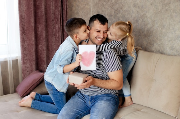 Famiglia felice, figlia e figlio danno un regalo e una carta al padre per le vacanze.