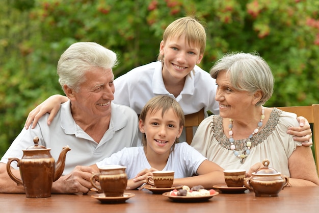 Happy family drinking tea at table outdoors in summer time