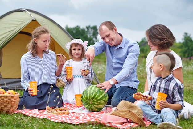 Happy family eating watermelon at picnic in meadow near the tent Family Enjoying Camping Holiday In Countryside