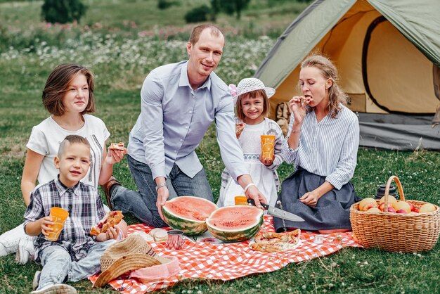 Famiglia felice che mangia anguria al picnic nel prato vicino alla tenda famiglia godendo le vacanze in campeggio in campagna