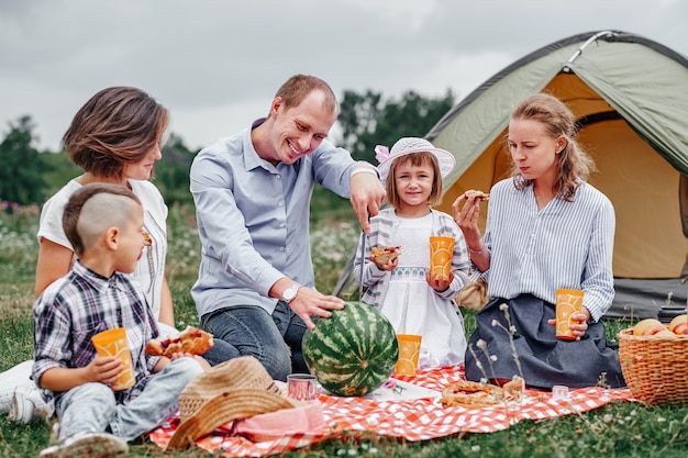 Happy family eating watermelon at picnic in meadow near the tent. Family Enjoying Camping Holiday In Countryside.