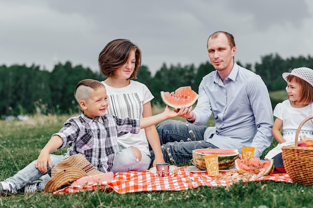 牧草地や公園でのピクニックでスイカを食べる幸せな家族若い友人と自然の中で彼らの子供たち