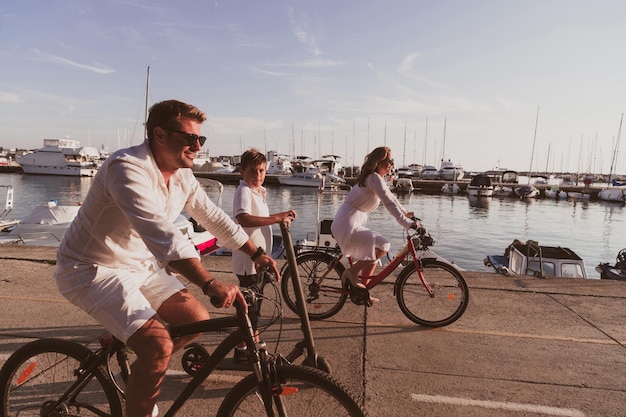 Счастливая семья наслаждается прекрасным утром у моря вместе, родители катаются на велосипеде, а их сын ри