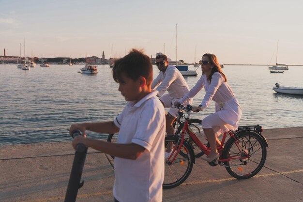 幸せな家族が一緒に海辺で美しい朝を楽しんでいます 自転車に乗っている両親と電気スクーターに乗っている息子 選択的な焦点