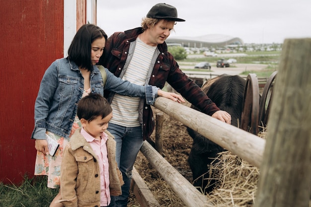 Happy family on the farm petting pony family day young father mother and son are outdoors enjoying b