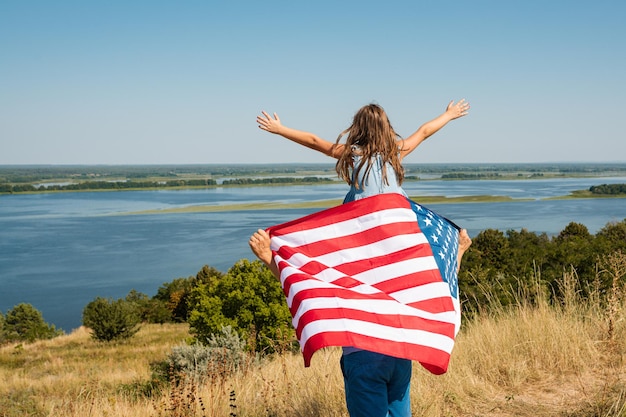 写真 自然の中で夕日を楽しむ幸せな家族の父と米国旗を持つ子供