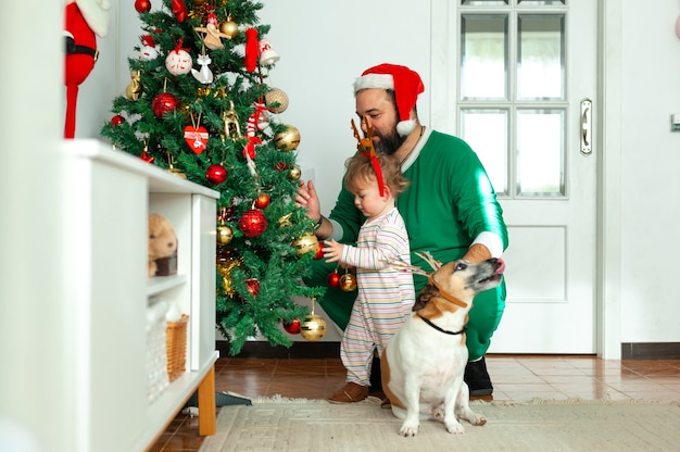 幸せな家族の父子娘と犬がクリスマスツリーを飾る