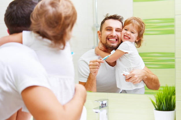 Happy family father and child girl brushing her teeth in bathroom