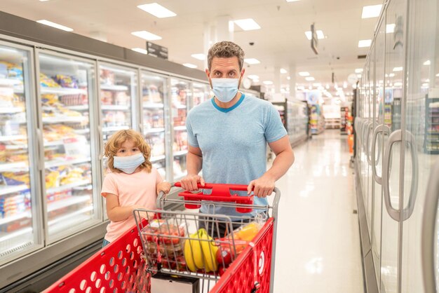 Happy family of father and child in protection mask with shopping cart buying food, consumption