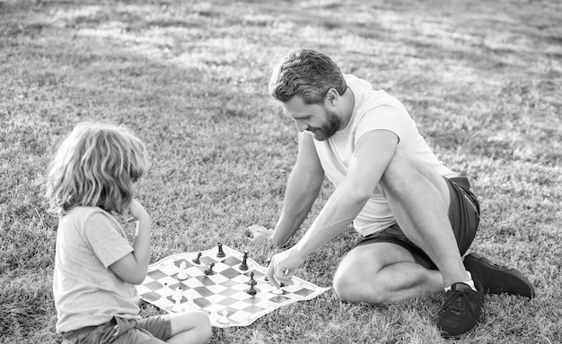 Happy family of father man and son child playing chess on green grass in park outdoor strategy