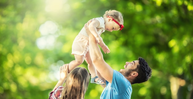 Счастливая семья, отец, мать и дочь играют в парке и наслаждаются солнечным летним днем.
