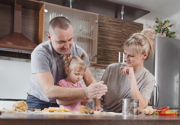 Famiglia felice, padre, madre e figlia piccola preparano insieme deliziosi biscotti pasquali nella cucina di casa. preparazione per le vacanze in famiglia