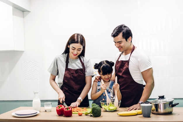 Happy family father and mother with daughter cooking and preparing meal