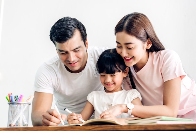 Happy family father and mother with daughter  learning and writing in notebook with pencil making homework at home.Education concept